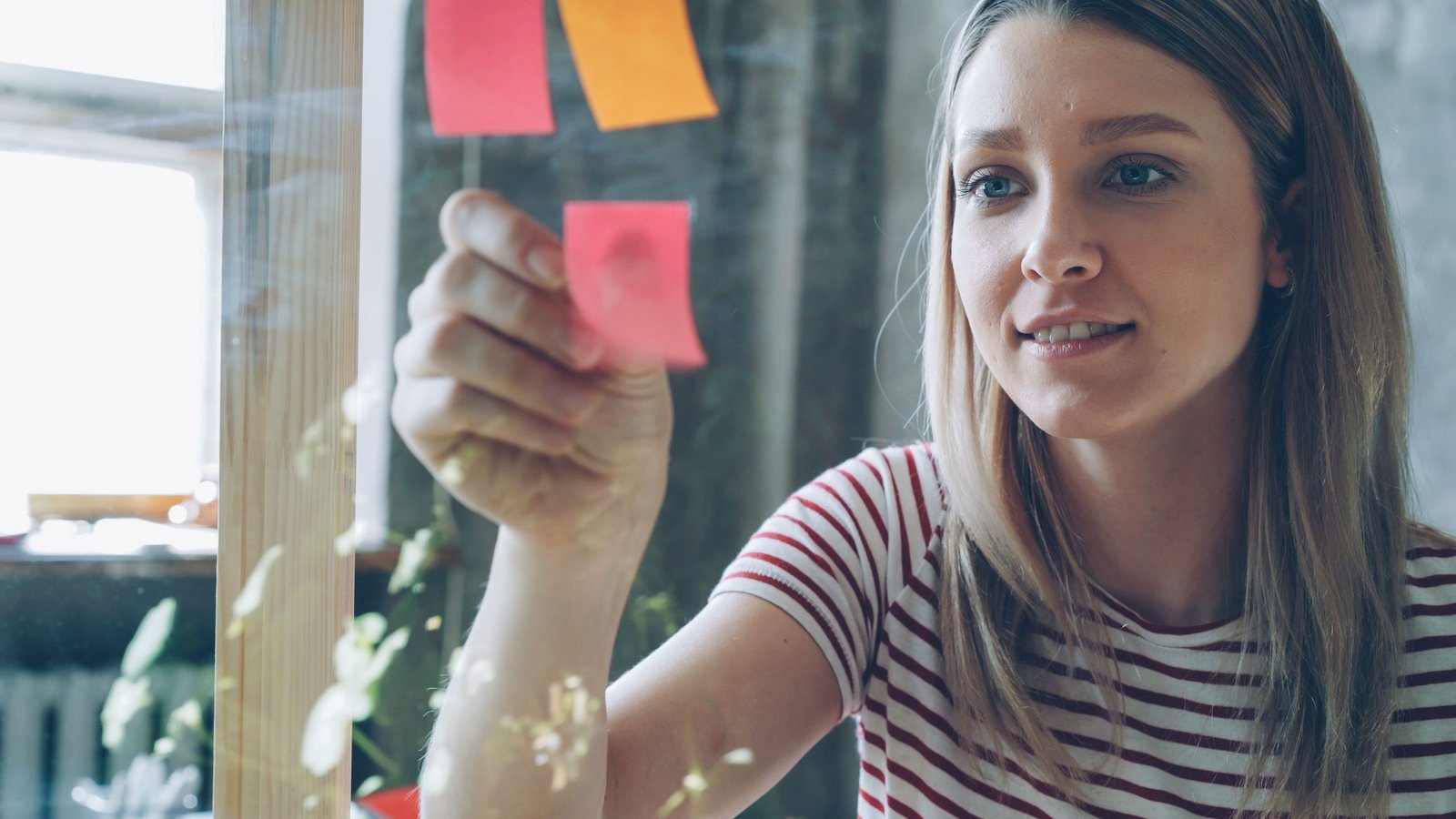 Focused young woman organizing ideas on sticky notes in a bright office environment.